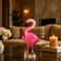 Pink flamingo figurine on a table with dimensions displayed, set against a blurred indoor background.